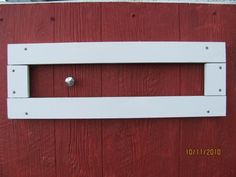 a red and white door with a metal handle on it's side, in front of a wooden wall