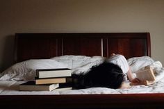 a woman laying on top of a bed next to two stacks of books in front of her