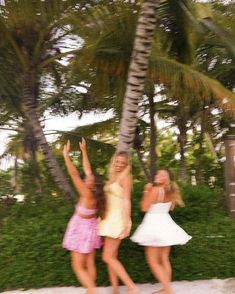 two young women standing next to each other in front of palm trees on the beach