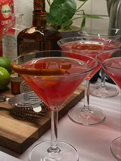 two martini glasses filled with red liquid and garnished with an orange peel on a cutting board