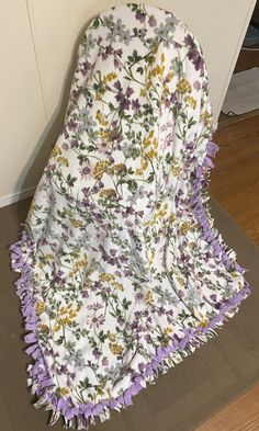 a white and purple blanket sitting on top of a wooden floor next to a wall