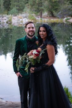 a man and woman standing next to each other in front of a lake holding flowers