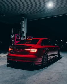 a red car parked in front of a gas station at night with its lights on