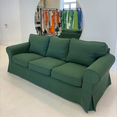 a green couch in front of a mirror with clothes hanging on the rack behind it