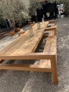 a long wooden table sitting in the middle of a gravel covered area next to trees