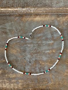 a white beaded necklace with red, green and blue beads on a wooden surface