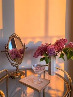 a glass table with flowers and a mirror on the top, in front of a window