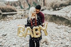 a man and woman standing on rocks with the words baby spelled in gold