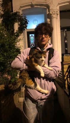 a man is holding a cat in his arms outside at night with the lights on