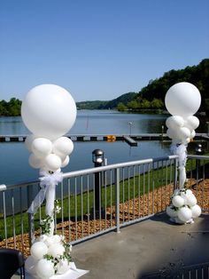 some white balloons are on the side of a railing near water and trees in the background