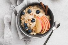 a bowl filled with oatmeal, apples and blueberries next to a spoon