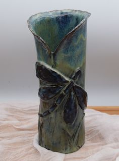 a green vase sitting on top of a white cloth covered table next to a wall