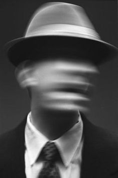 a blurry image of a man wearing a suit and tie with a hat on his head