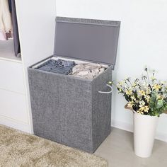 an open suitcase sitting on the floor next to a flower pot with clothes in it