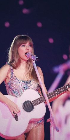 a woman holding a guitar and singing into a microphone