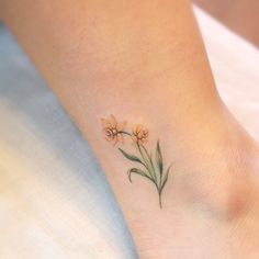 a small flower tattoo on the foot of a woman's left ankle, with yellow flowers