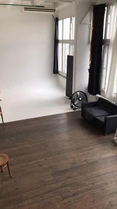 an empty living room with wood floors and black furniture in front of two large windows