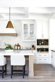 a kitchen with white cabinets and marble counter tops, two stools at the island