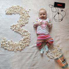 a baby laying on top of a bed next to popcorn