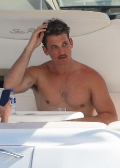 a shirtless man sitting at a table on top of a white boat next to another person