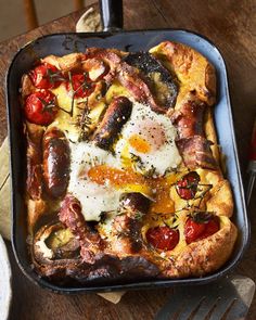 an egg and sausage pizza in a pan on a wooden table with utensils