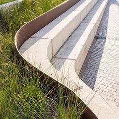 a bench sitting on top of a brick walkway next to tall grass and trees in the background