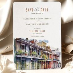 a wedding save the date card with an image of buildings on it and flowers in front