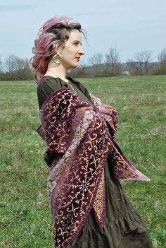 a woman standing in a field wearing a purple and green shawl with flowers on it