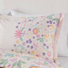 a white bed topped with pillows covered in colorful floral sheets and pillowcases on top of a wooden headboard