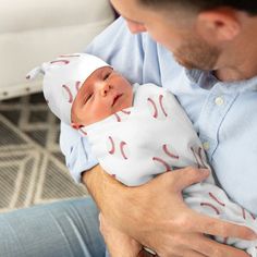 a man holding a baby wearing a baseball hat and sleeping on it's back