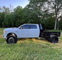 a large white truck parked on top of a grass covered field with trees in the background