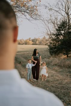 a woman and two children are standing in the grass with their mother looking at them