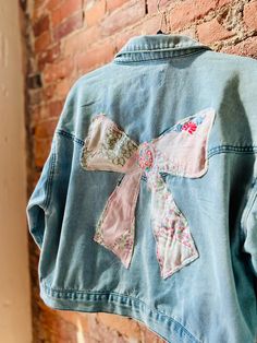 an old jean jacket with a pink bow on it hanging from a brick wall in front of a brick wall