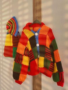 a colorful knitted sweater hanging on a wooden pole next to a shadow cast wall