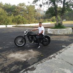 a man sitting on his motorcycle in the middle of an empty parking lot next to a tree