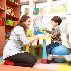 a woman playing with a child on an exercise ball in a room full of children's toys