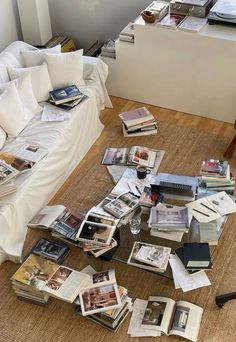 a pile of books sitting on top of a wooden floor next to a white couch