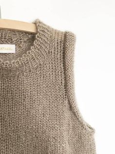 a sweater hanging on a wooden hanger next to a white wall with a tag