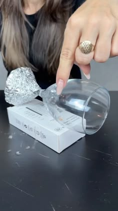 a woman pointing at something in a plastic container on top of a table next to a box