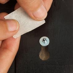 a person holding a piece of paper with a screw in the middle of it next to a button