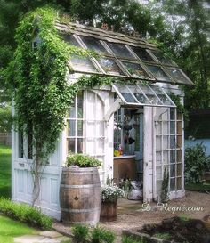 an old greenhouse with vines growing on the roof and doors, in front of a house