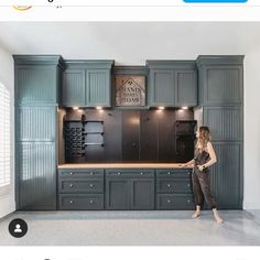 a woman standing in front of a kitchen with green cupboards and an oven on the wall