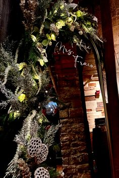 a decorated christmas tree in front of a brick wall with the words merry christmas written on it