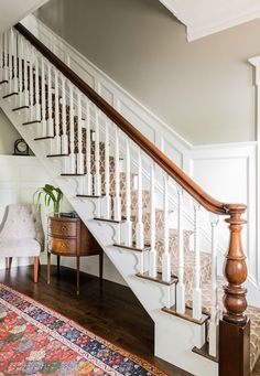 a white staircase with wooden handrails next to a chair and rug on the floor