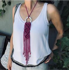 a woman wearing a white tank top with a red tasseled necklace on her neck