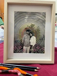 two people standing in front of a picture with pencils on the table next to it