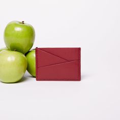 two green apples sitting next to an apple with a red leather card case on it