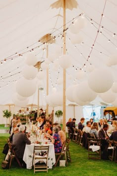 a group of people sitting at tables in a tent with lights strung from the ceiling