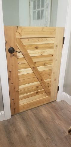 a wooden door with a metal latch on it's side in a room that has hardwood floors and white walls