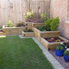 several wooden planters with flowers in them near a brick wall and green grass on the ground